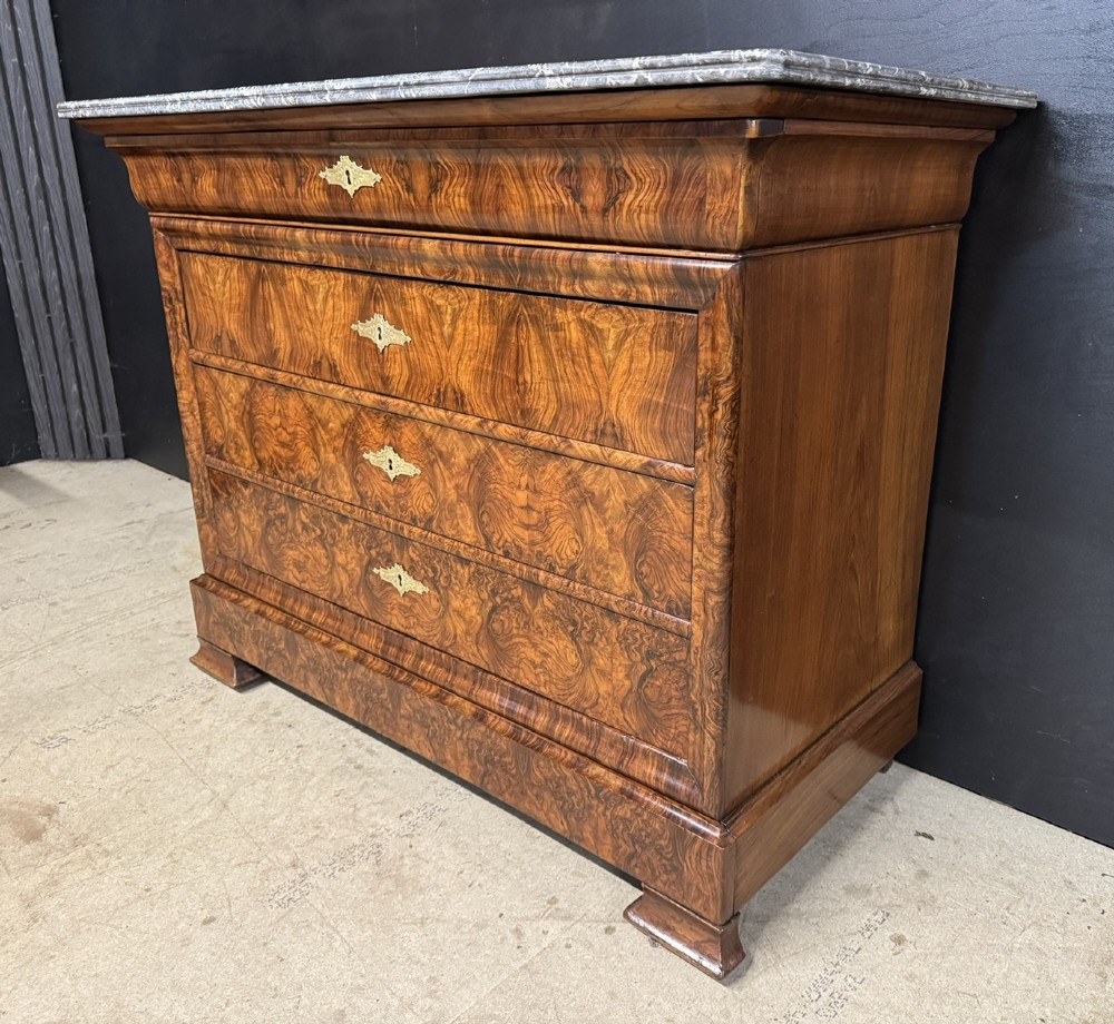 A 19th-century French Louis Philippe burr walnut commode featuring a grey marble top, four drawers, and ornate brass keyhole escutcheons. View X
