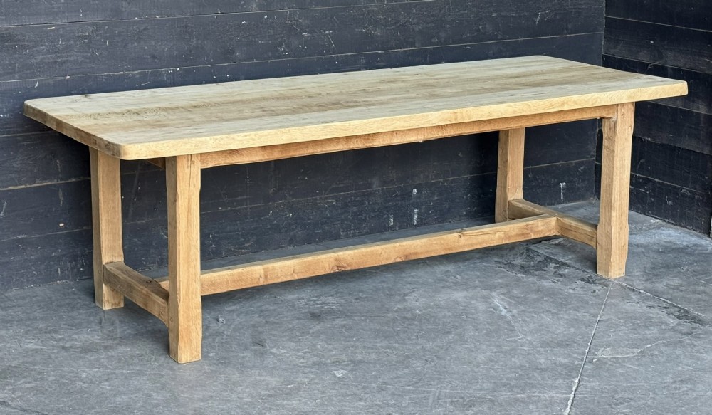 A large rectangular natural oak farmhouse dining table featuring a thick plank top, square legs, and an H-stretcher base.