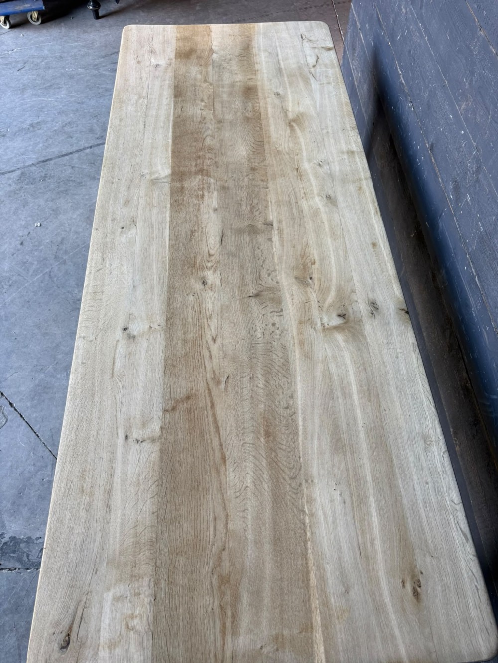 A large rectangular natural oak farmhouse dining table featuring a thick plank top, square legs, and an H-stretcher base. View VI