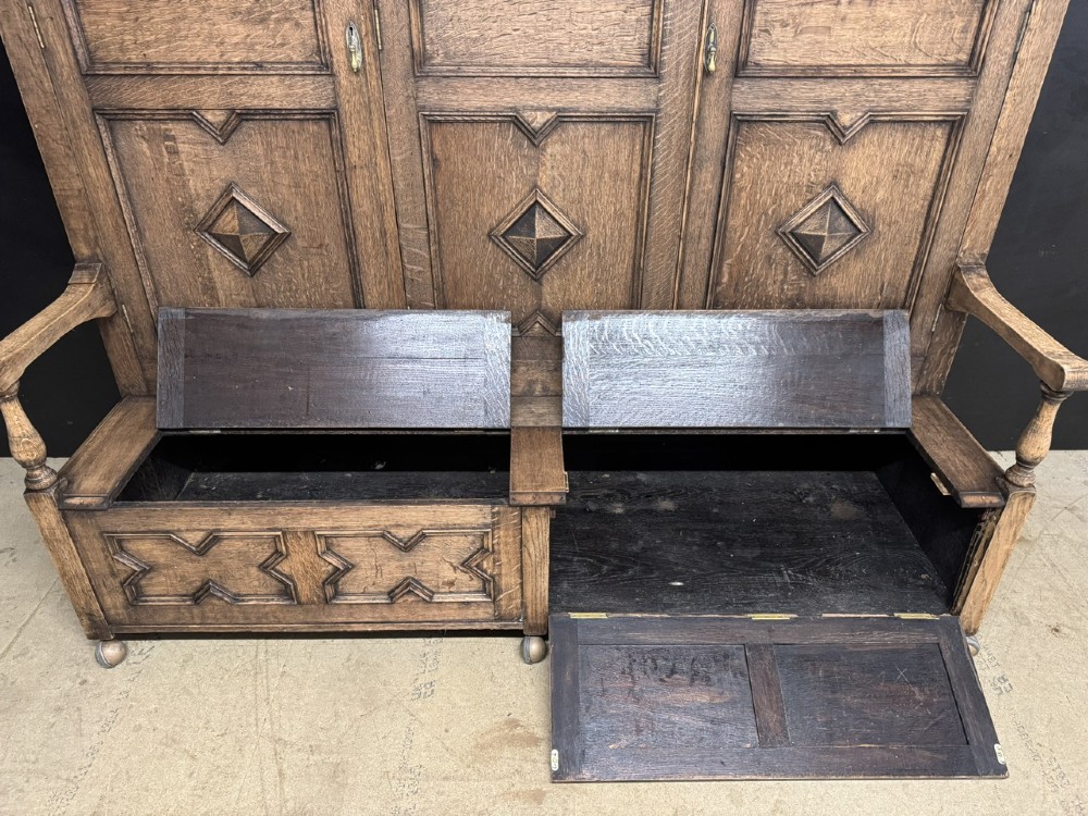 A large carved oak hall bench featuring a high back with three cupboard doors, geometric diamond panelling, and a lift-top storage seat. View III