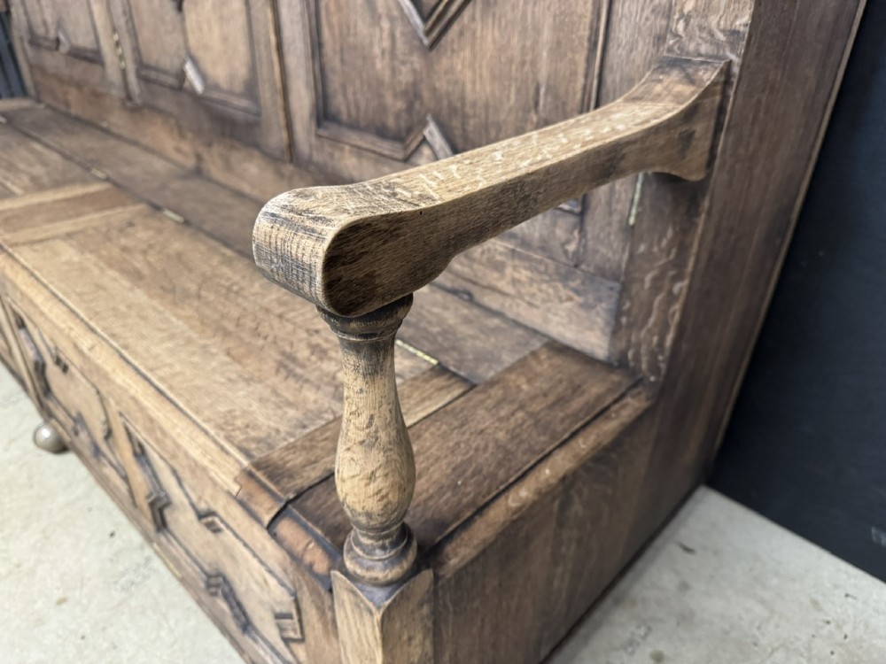 A large carved oak hall bench featuring a high back with three cupboard doors, geometric diamond panelling, and a lift-top storage seat. View VIII