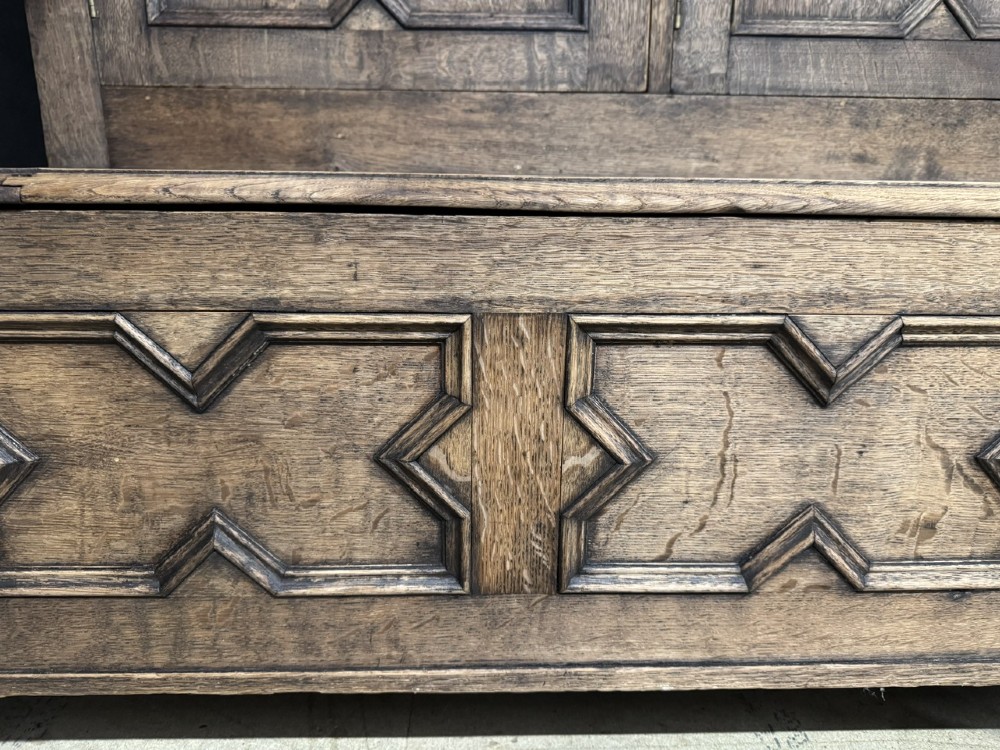 A large carved oak hall bench featuring a high back with three cupboard doors, geometric diamond panelling, and a lift-top storage seat. View IX