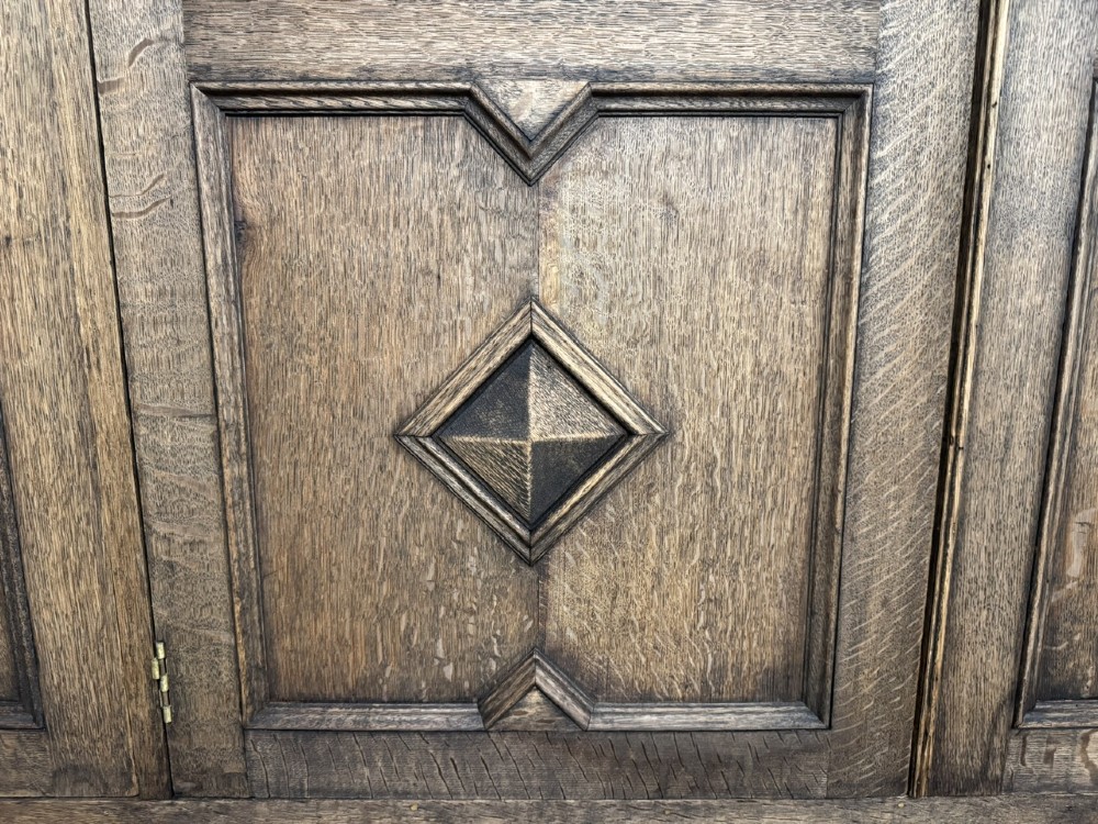 A large carved oak hall bench featuring a high back with three cupboard doors, geometric diamond panelling, and a lift-top storage seat. View X