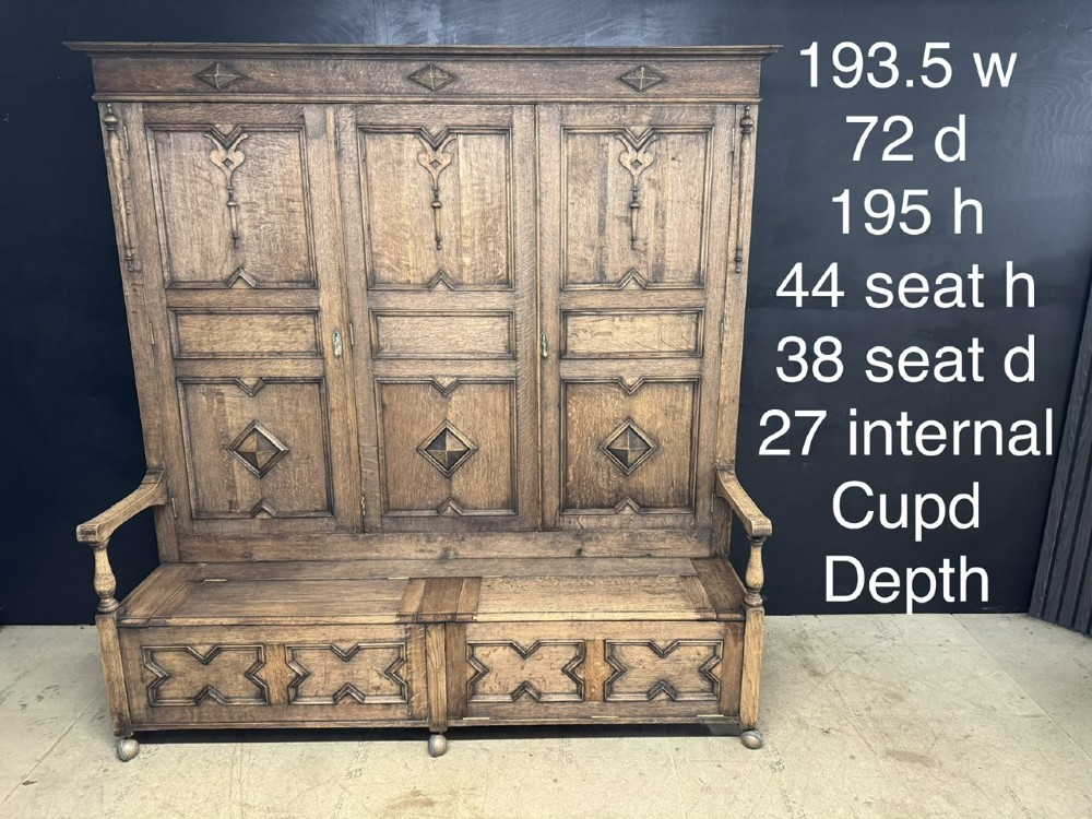 A large carved oak hall bench featuring a high back with three cupboard doors, geometric diamond panelling, and a lift-top storage seat. View XII