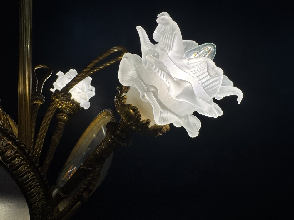 An ornate French gilt bronze chandelier featuring scroll arms, cut glass inserts, and ruffled white glass flower shades. View III