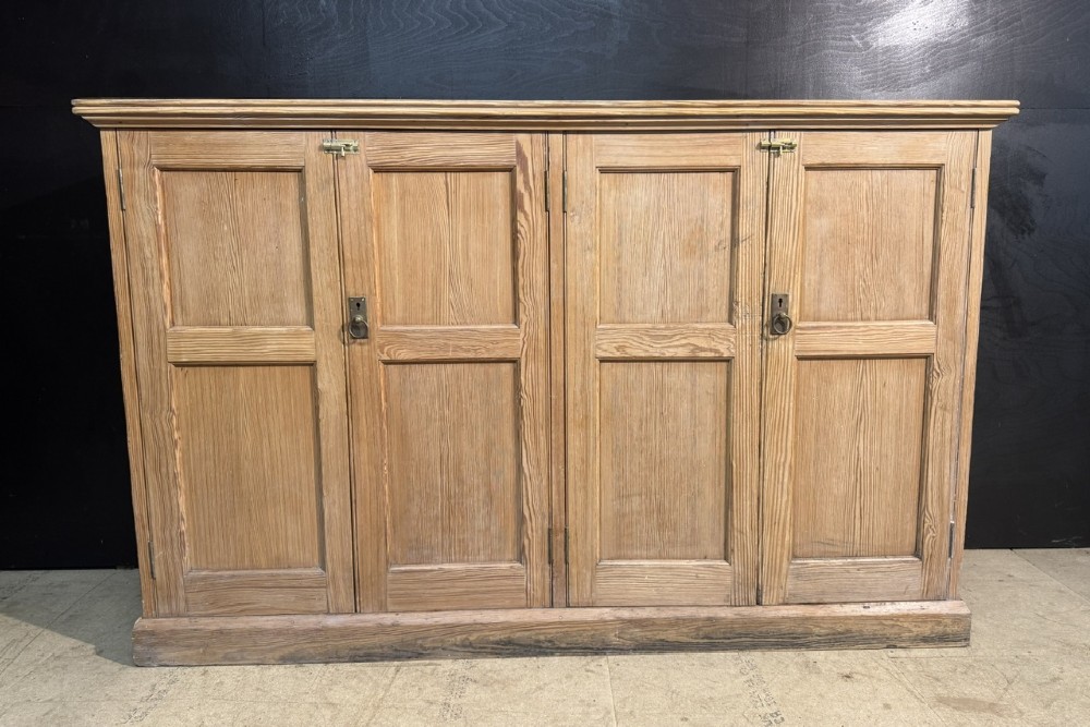 A 19th-century natural pine housekeepers cupboard featuring four panelled doors with brass drop handles and a plinth base.