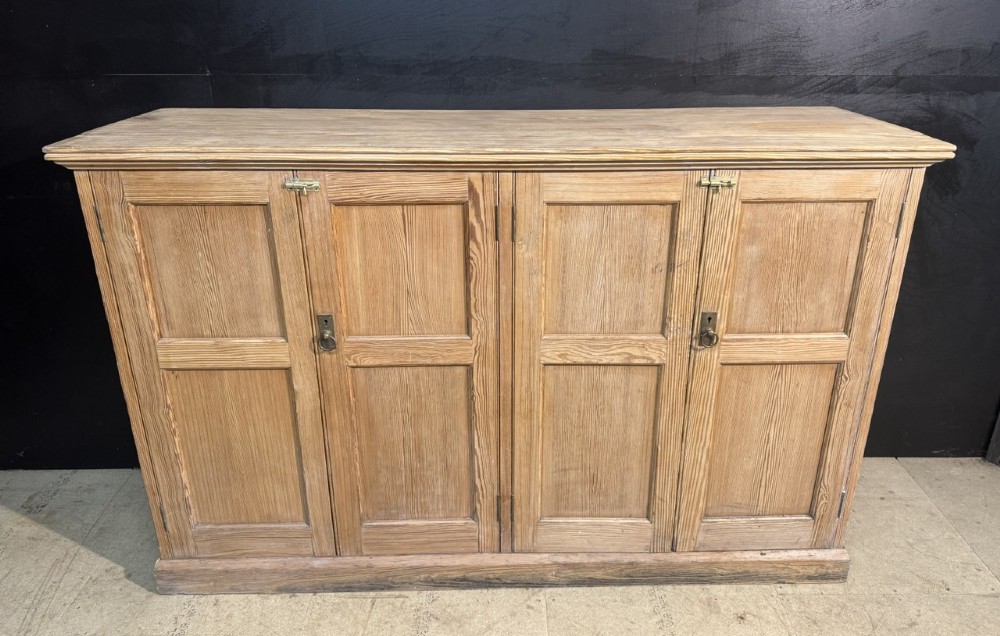 A 19th-century natural pine housekeepers cupboard featuring four panelled doors with brass drop handles and a plinth base. View II
