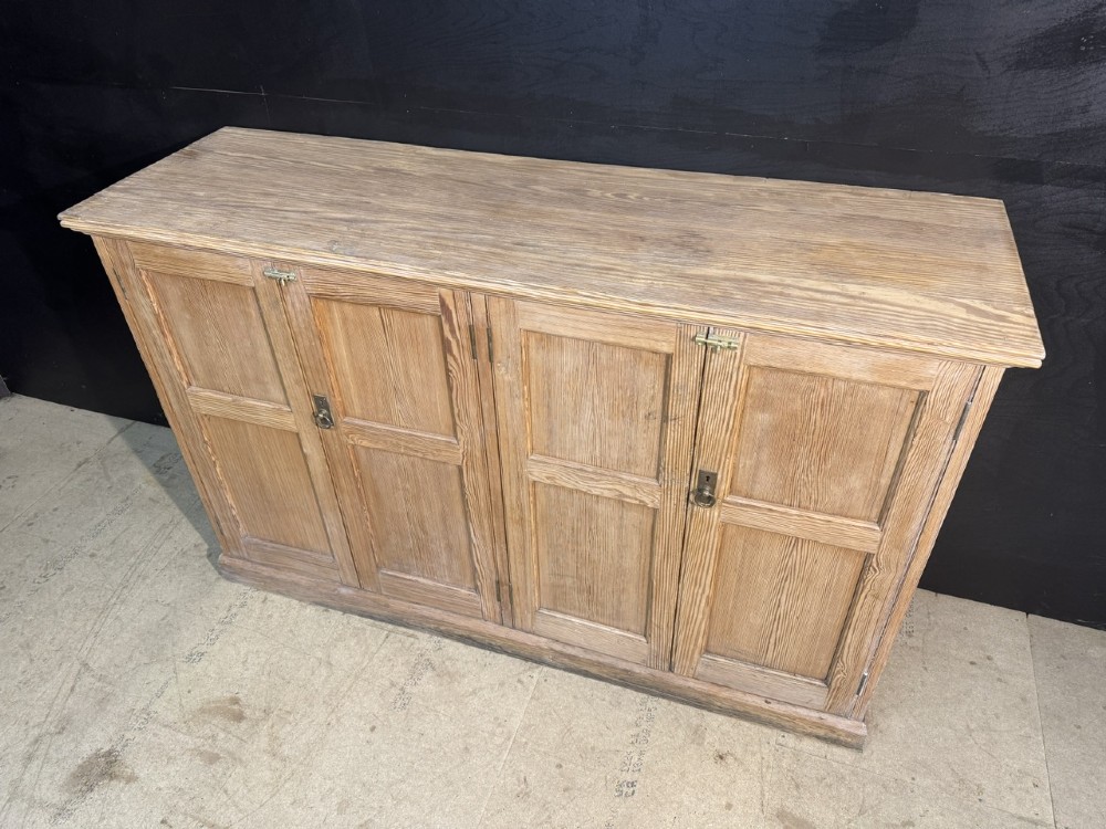 A 19th-century natural pine housekeepers cupboard featuring four panelled doors with brass drop handles and a plinth base. View III