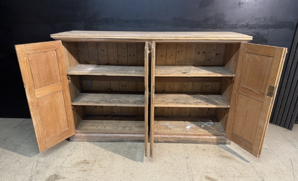A 19th-century natural pine housekeepers cupboard featuring four panelled doors with brass drop handles and a plinth base. View IV