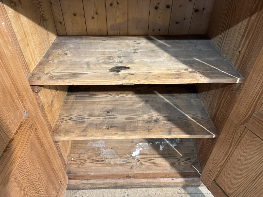 A 19th-century natural pine housekeepers cupboard featuring four panelled doors with brass drop handles and a plinth base. View V