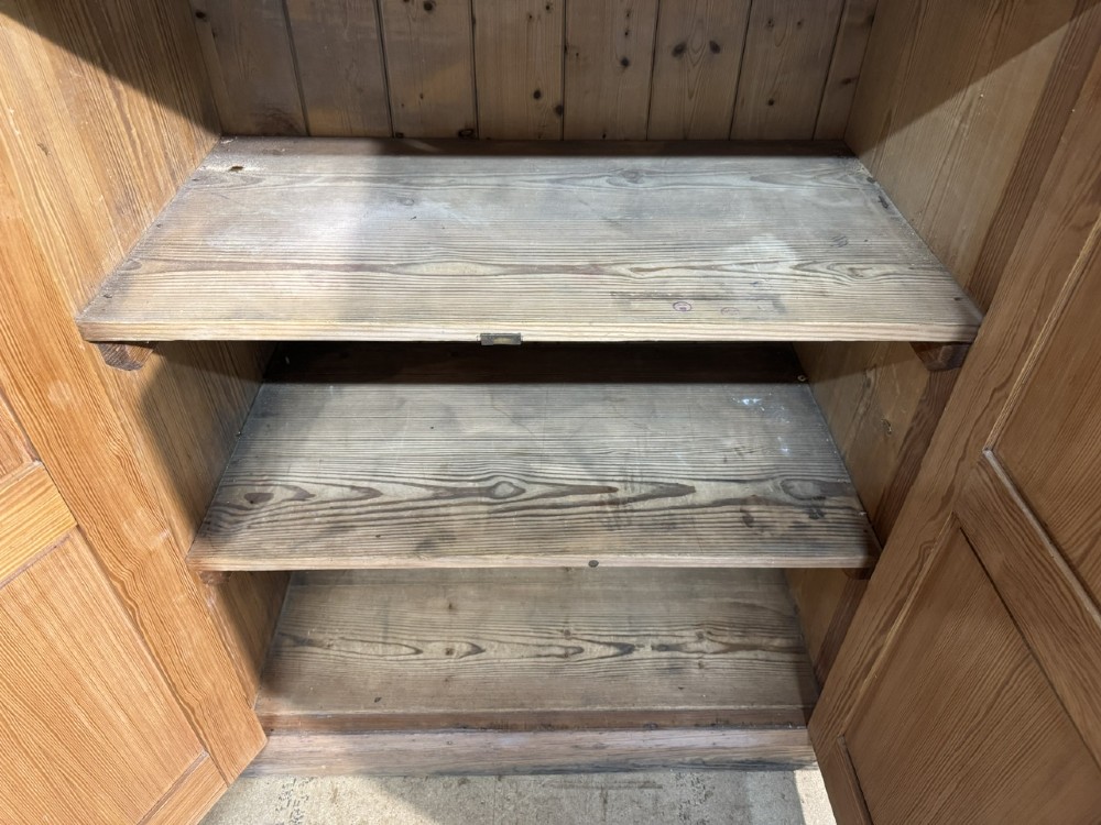 A 19th-century natural pine housekeepers cupboard featuring four panelled doors with brass drop handles and a plinth base. View VI