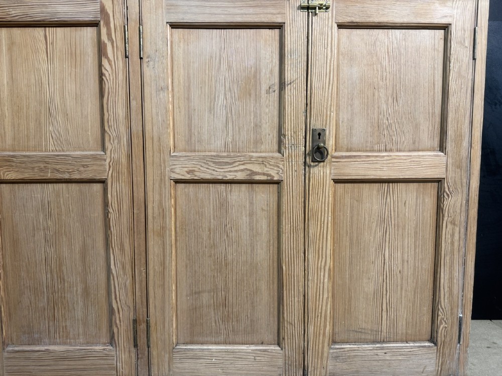 A 19th-century natural pine housekeepers cupboard featuring four panelled doors with brass drop handles and a plinth base. View VII