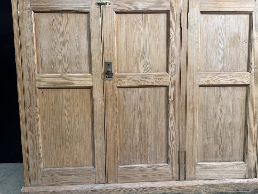 A 19th-century natural pine housekeepers cupboard featuring four panelled doors with brass drop handles and a plinth base. View VIII