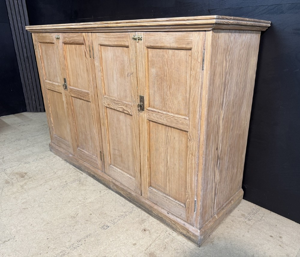 A 19th-century natural pine housekeepers cupboard featuring four panelled doors with brass drop handles and a plinth base. View IX