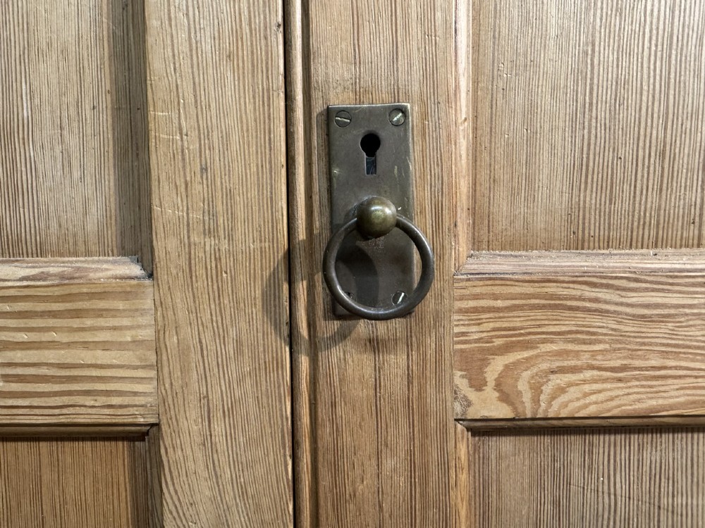 A 19th-century natural pine housekeepers cupboard featuring four panelled doors with brass drop handles and a plinth base. View XI