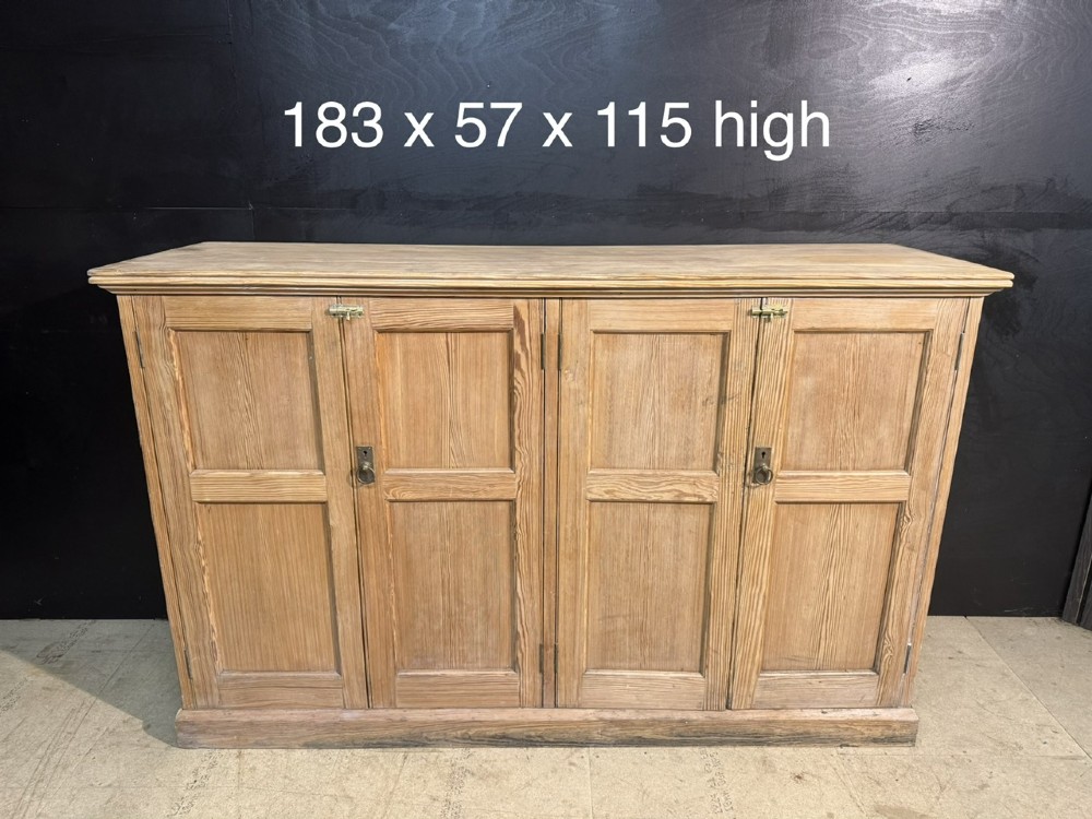 A 19th-century natural pine housekeepers cupboard featuring four panelled doors with brass drop handles and a plinth base. View XV
