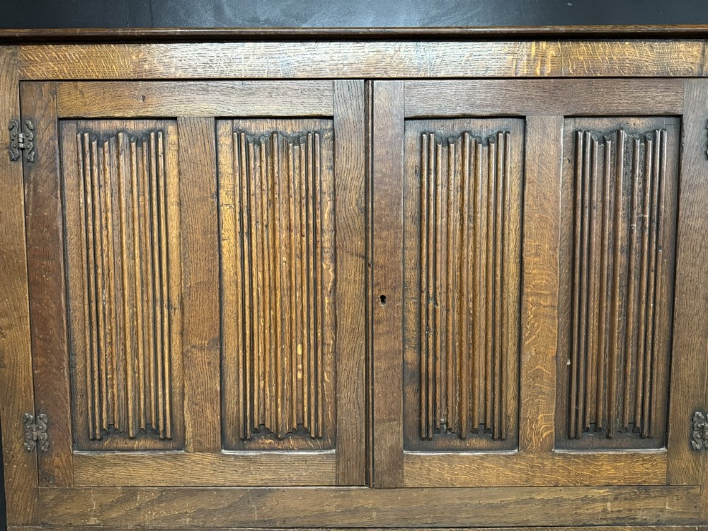 A narrow dark oak hall cupboard featuring upper carved linenfold doors and lower plain panel doors with iron hinges. View II