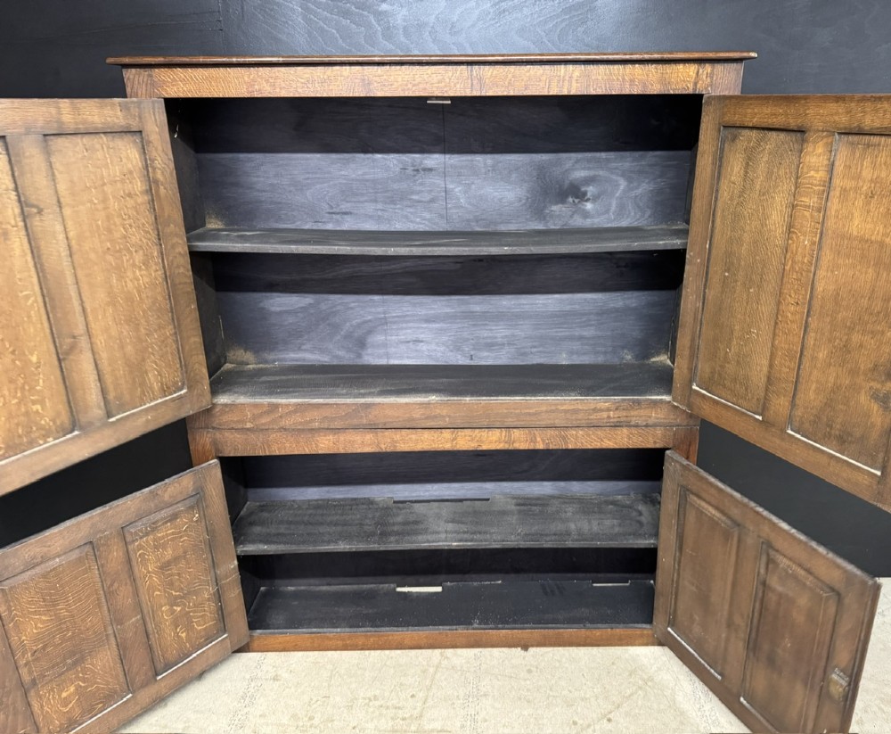 A narrow dark oak hall cupboard featuring upper carved linenfold doors and lower plain panel doors with iron hinges. View V