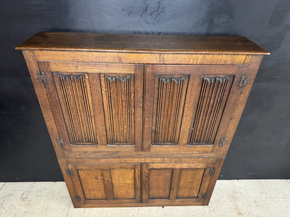 A narrow dark oak hall cupboard featuring upper carved linenfold doors and lower plain panel doors with iron hinges. View VII