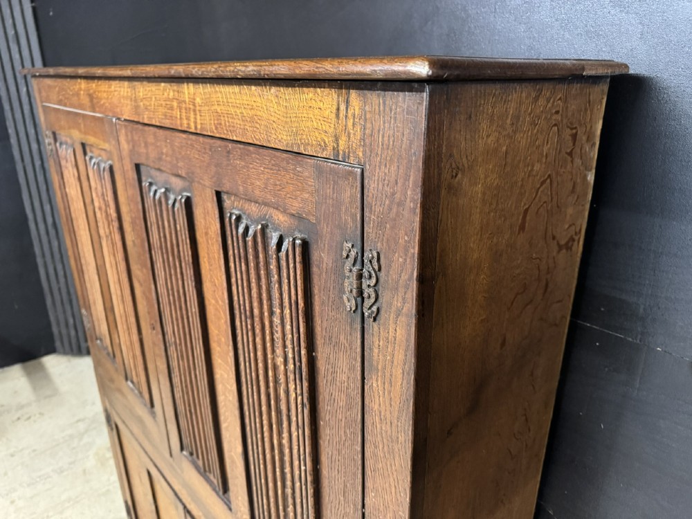 A narrow dark oak hall cupboard featuring upper carved linenfold doors and lower plain panel doors with iron hinges. View X
