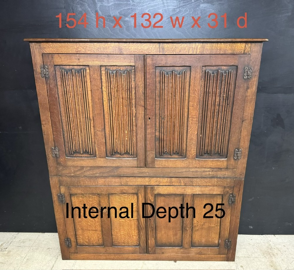 A narrow dark oak hall cupboard featuring upper carved linenfold doors and lower plain panel doors with iron hinges. View XI