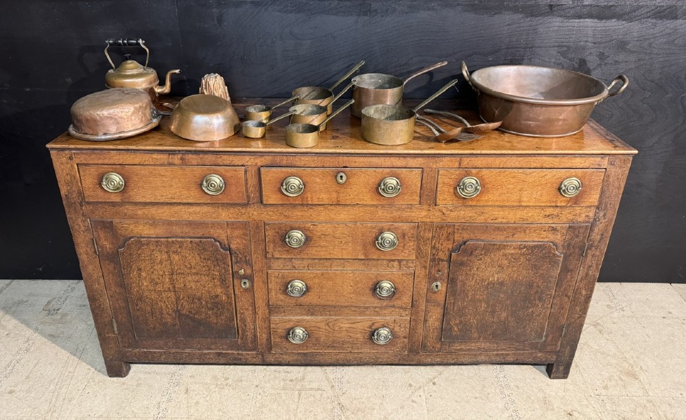 A Georgian Welsh oak dresser base with multiple drawers and two panelled cupboard doors featuring brass drop handles. View II
