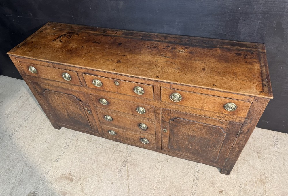 A Georgian Welsh oak dresser base with multiple drawers and two panelled cupboard doors featuring brass drop handles. View III