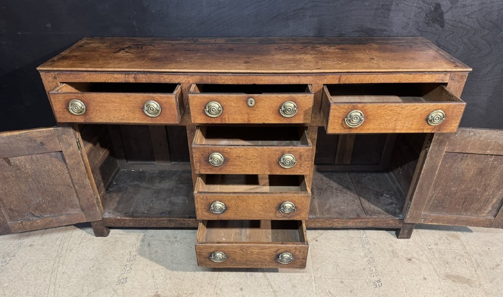 A Georgian Welsh oak dresser base with multiple drawers and two panelled cupboard doors featuring brass drop handles. View IV