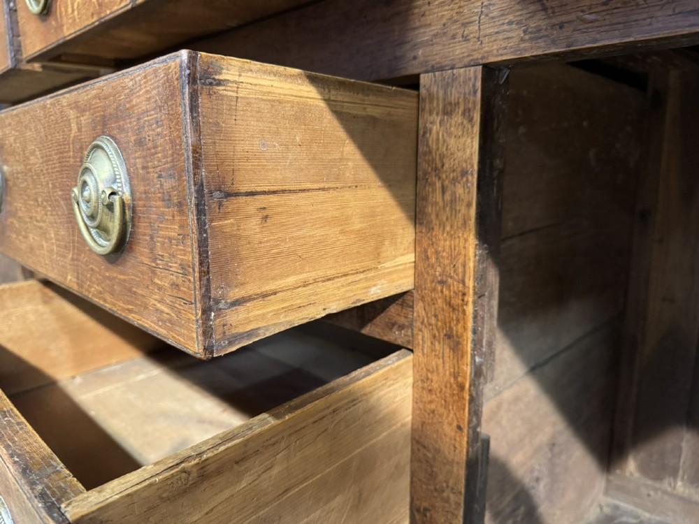 A Georgian Welsh oak dresser base with multiple drawers and two panelled cupboard doors featuring brass drop handles. View VI