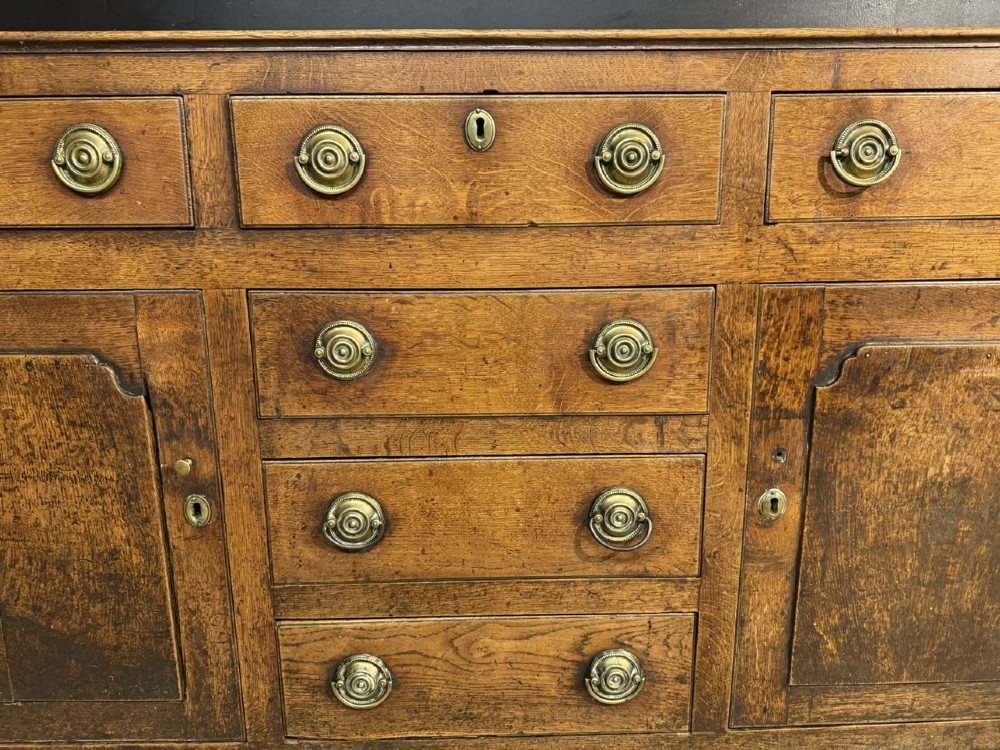 A Georgian Welsh oak dresser base with multiple drawers and two panelled cupboard doors featuring brass drop handles. View VIII