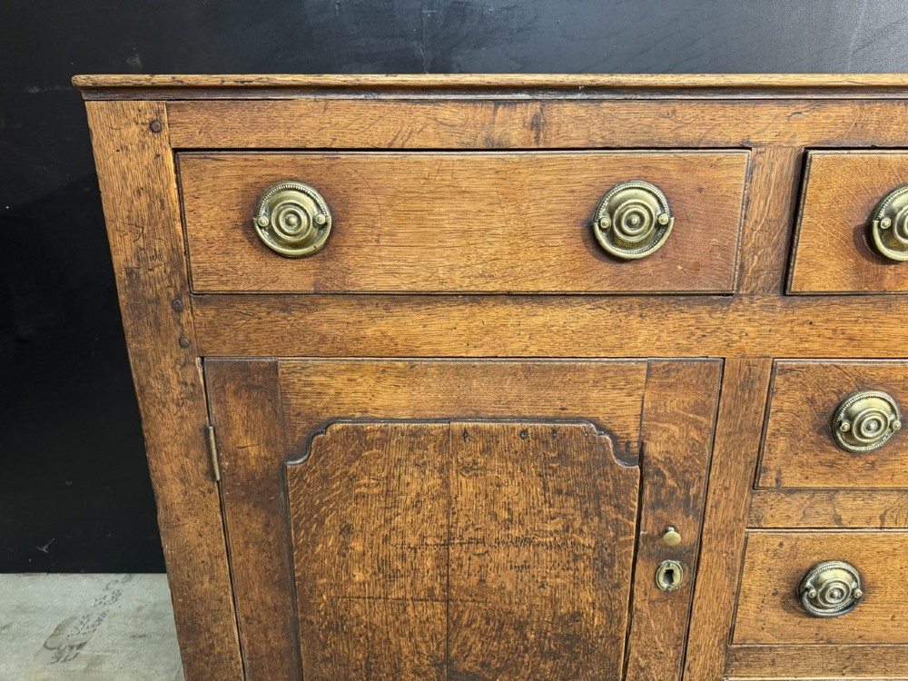 A Georgian Welsh oak dresser base with multiple drawers and two panelled cupboard doors featuring brass drop handles. View IX