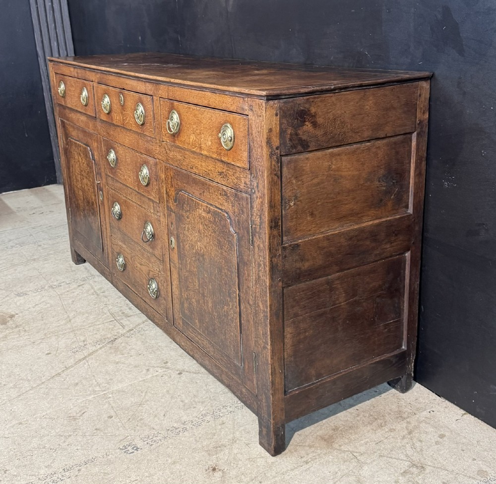 A Georgian Welsh oak dresser base with multiple drawers and two panelled cupboard doors featuring brass drop handles. View X