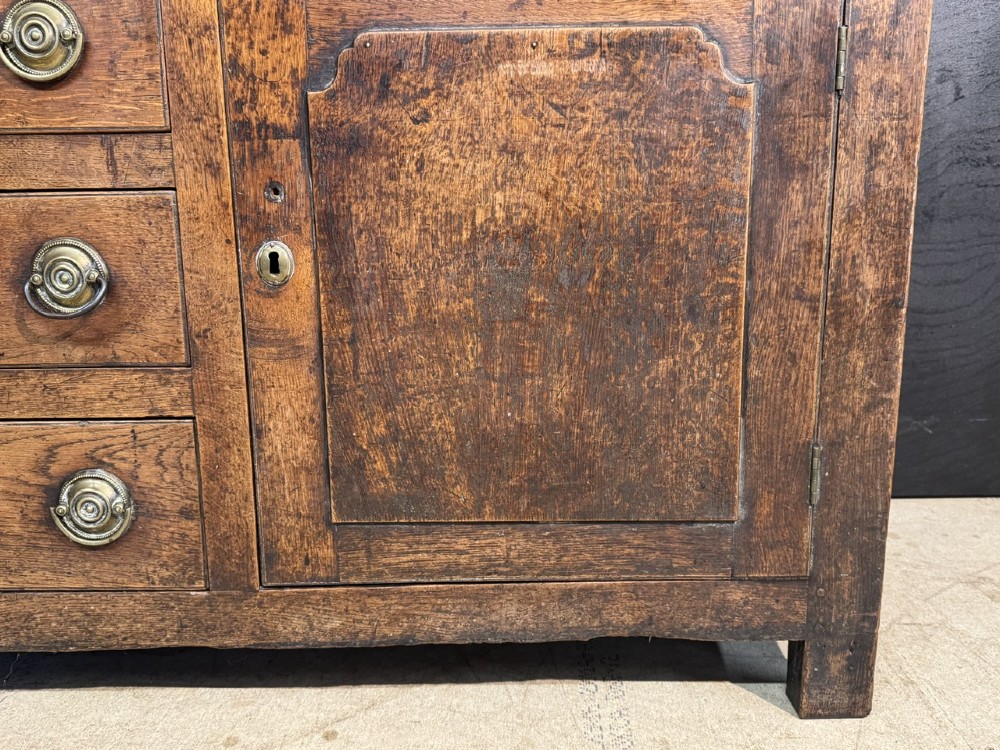 A Georgian Welsh oak dresser base with multiple drawers and two panelled cupboard doors featuring brass drop handles. View XII