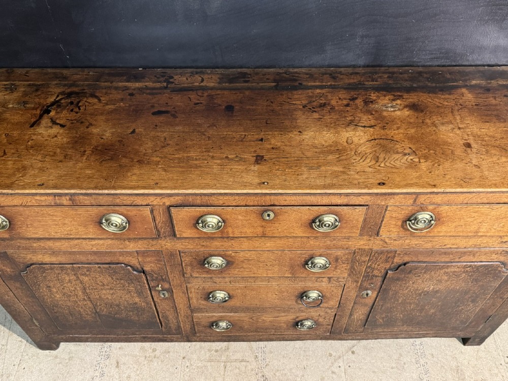 A Georgian Welsh oak dresser base with multiple drawers and two panelled cupboard doors featuring brass drop handles. View XIII