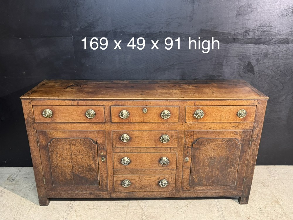 A Georgian Welsh oak dresser base with multiple drawers and two panelled cupboard doors featuring brass drop handles. View XIV