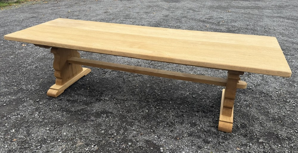 A three-metre-long natural oak trestle dining table featuring a solid plank top and a pegged central stretcher base.