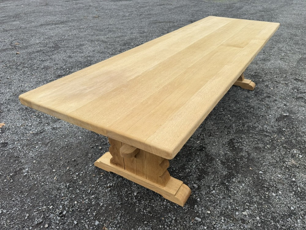 A three-metre-long natural oak trestle dining table featuring a solid plank top and a pegged central stretcher base. View V