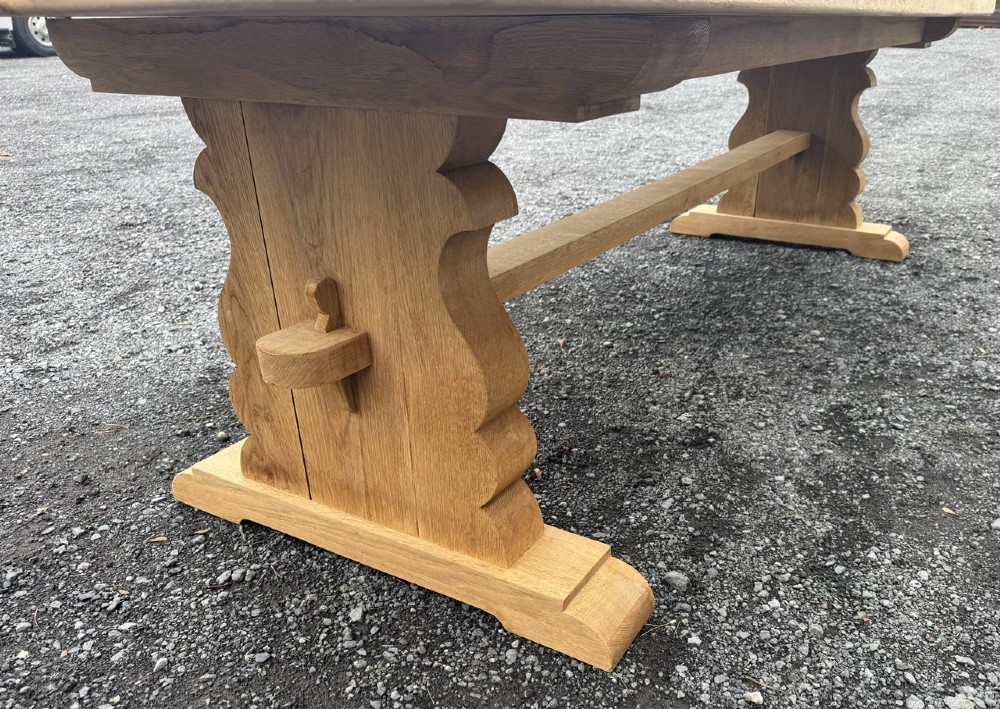A three-metre-long natural oak trestle dining table featuring a solid plank top and a pegged central stretcher base. View VI