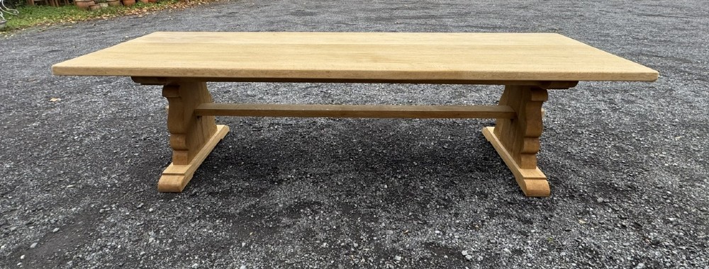 A three-metre-long natural oak trestle dining table featuring a solid plank top and a pegged central stretcher base. View X