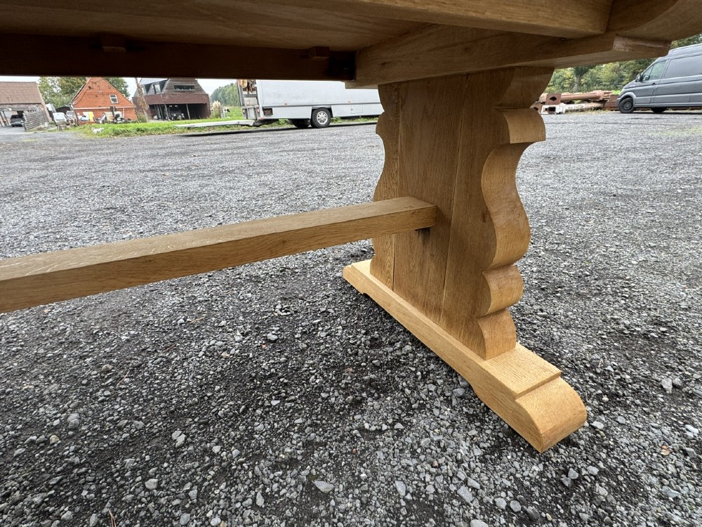 A three-metre-long natural oak trestle dining table featuring a solid plank top and a pegged central stretcher base. View XI
