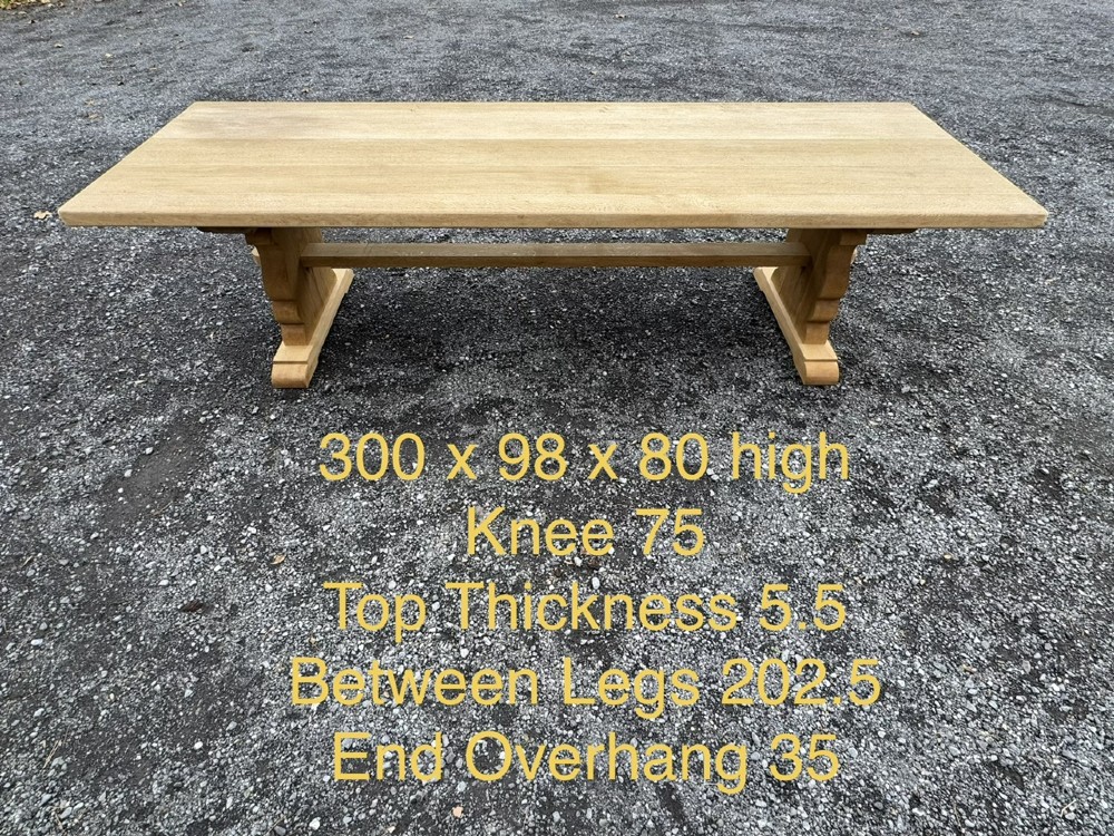 A three-metre-long natural oak trestle dining table featuring a solid plank top and a pegged central stretcher base. View XIII