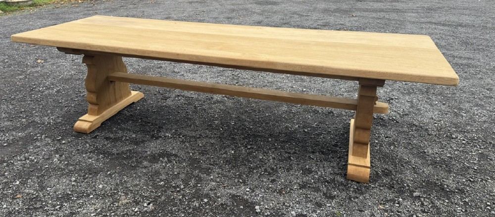 A three-metre-long natural oak trestle dining table featuring a solid plank top and a pegged central stretcher base. View XV