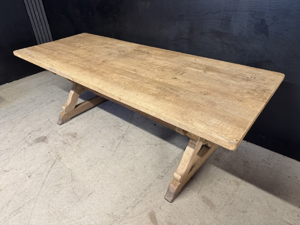 A rustic light oak dining table featuring a thick plank top supported by X-frame trestle legs and a pegged central stretcher. View II