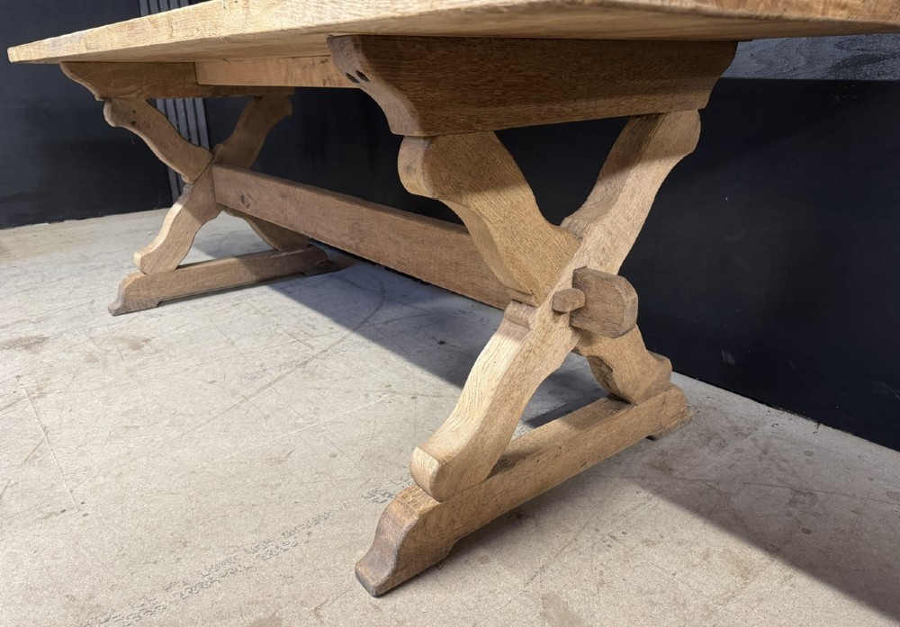 A rustic light oak dining table featuring a thick plank top supported by X-frame trestle legs and a pegged central stretcher. View III