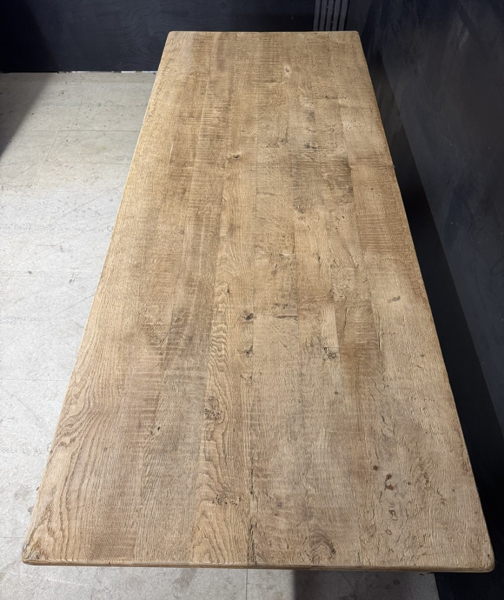 A rustic light oak dining table featuring a thick plank top supported by X-frame trestle legs and a pegged central stretcher. View IV