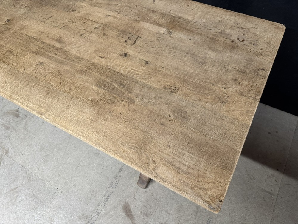 A rustic light oak dining table featuring a thick plank top supported by X-frame trestle legs and a pegged central stretcher. View VI