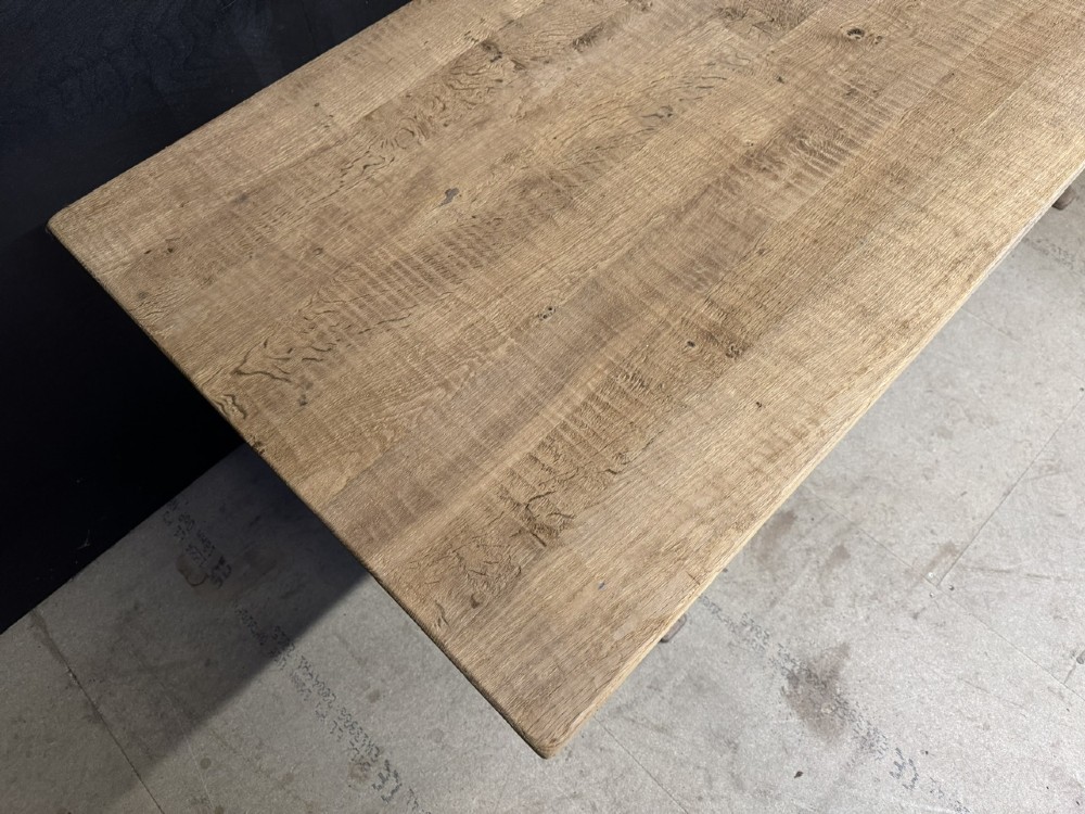 A rustic light oak dining table featuring a thick plank top supported by X-frame trestle legs and a pegged central stretcher. View VII