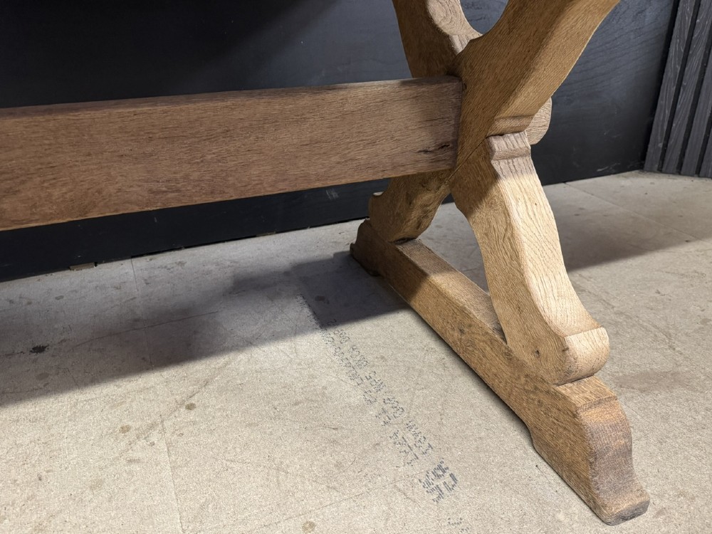 A rustic light oak dining table featuring a thick plank top supported by X-frame trestle legs and a pegged central stretcher. View IX