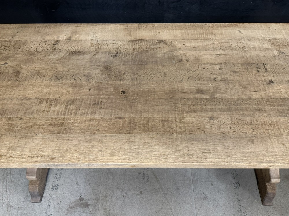 A rustic light oak dining table featuring a thick plank top supported by X-frame trestle legs and a pegged central stretcher. View X