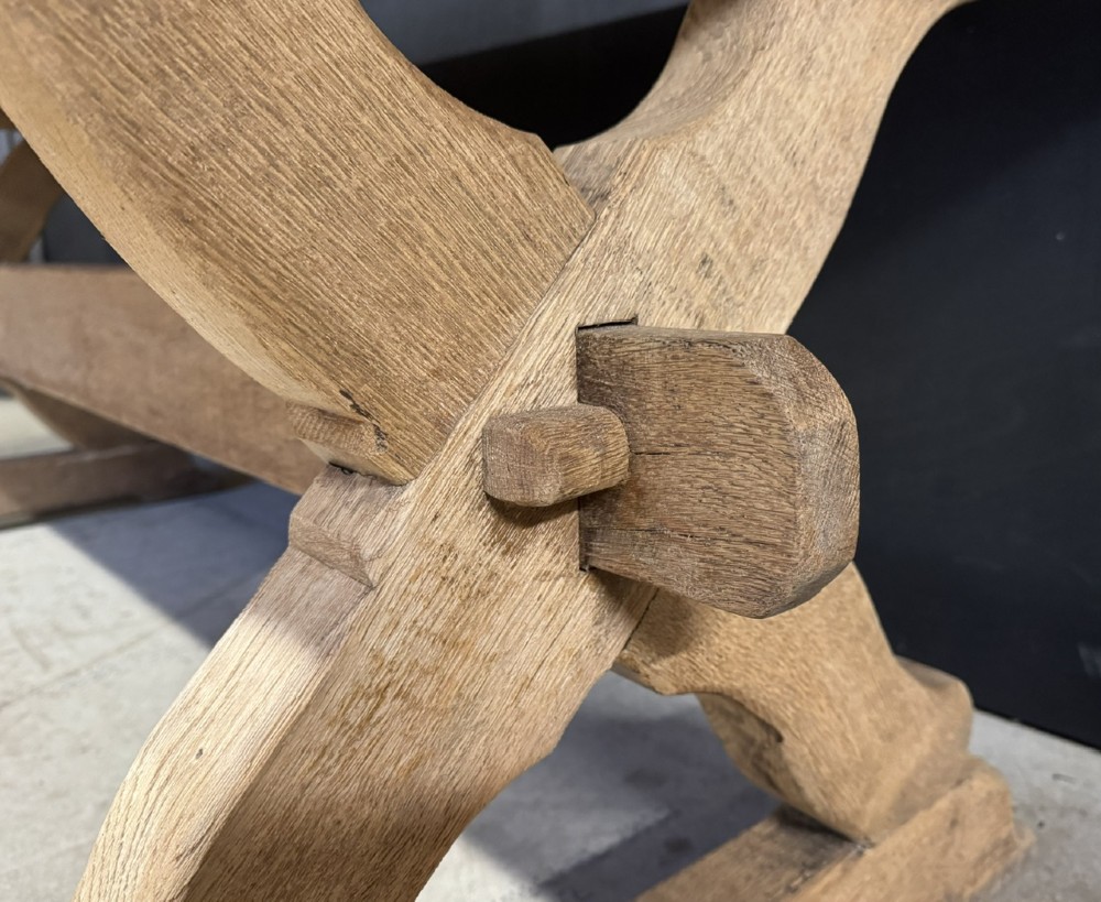 A rustic light oak dining table featuring a thick plank top supported by X-frame trestle legs and a pegged central stretcher. View XI